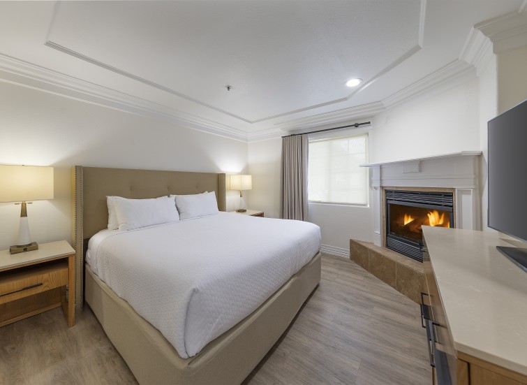 A hotel room with a king-size bed, a fireplace, and a flat-screen TV.