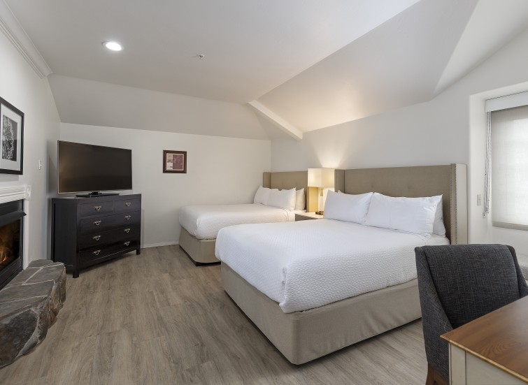 A hotel room with two beds, a fireplace, a TV, and a desk.