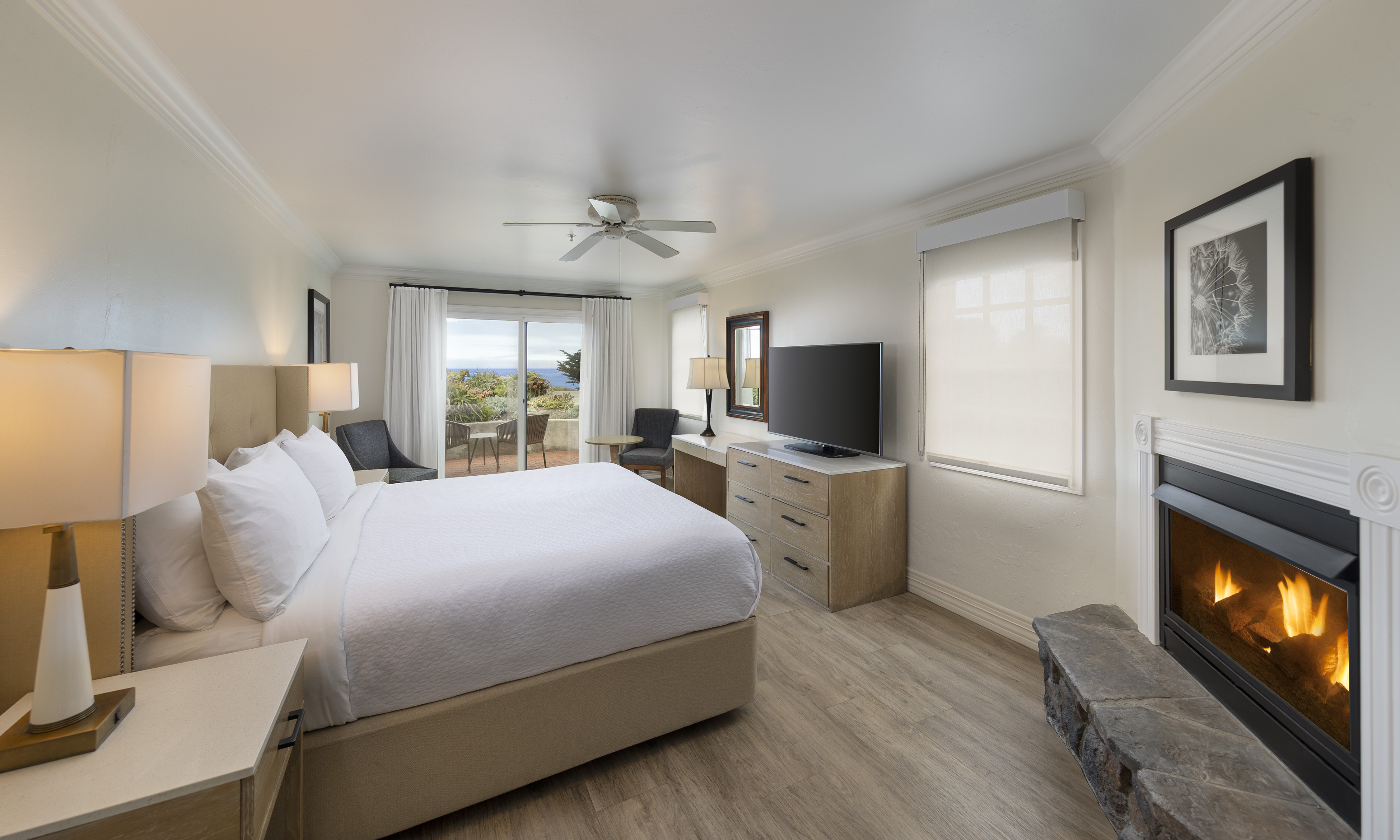A wide view of a hotel room with a bed, fireplace, TV, and balcony.