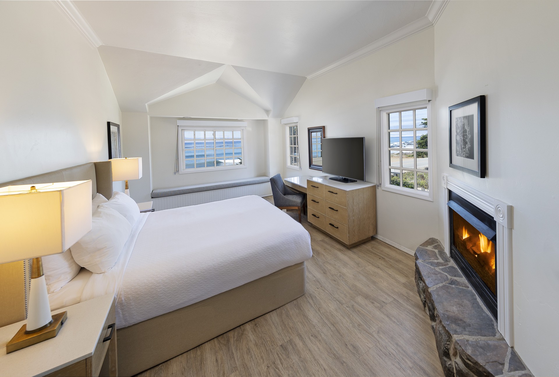 A wide view of a hotel room with a bed, fireplace, desk, and window seat.