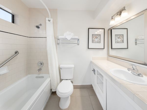 A clean bathroom with a bathtub/shower, toilet, dual-sink vanity, large mirror, framed art, and neutral tones.