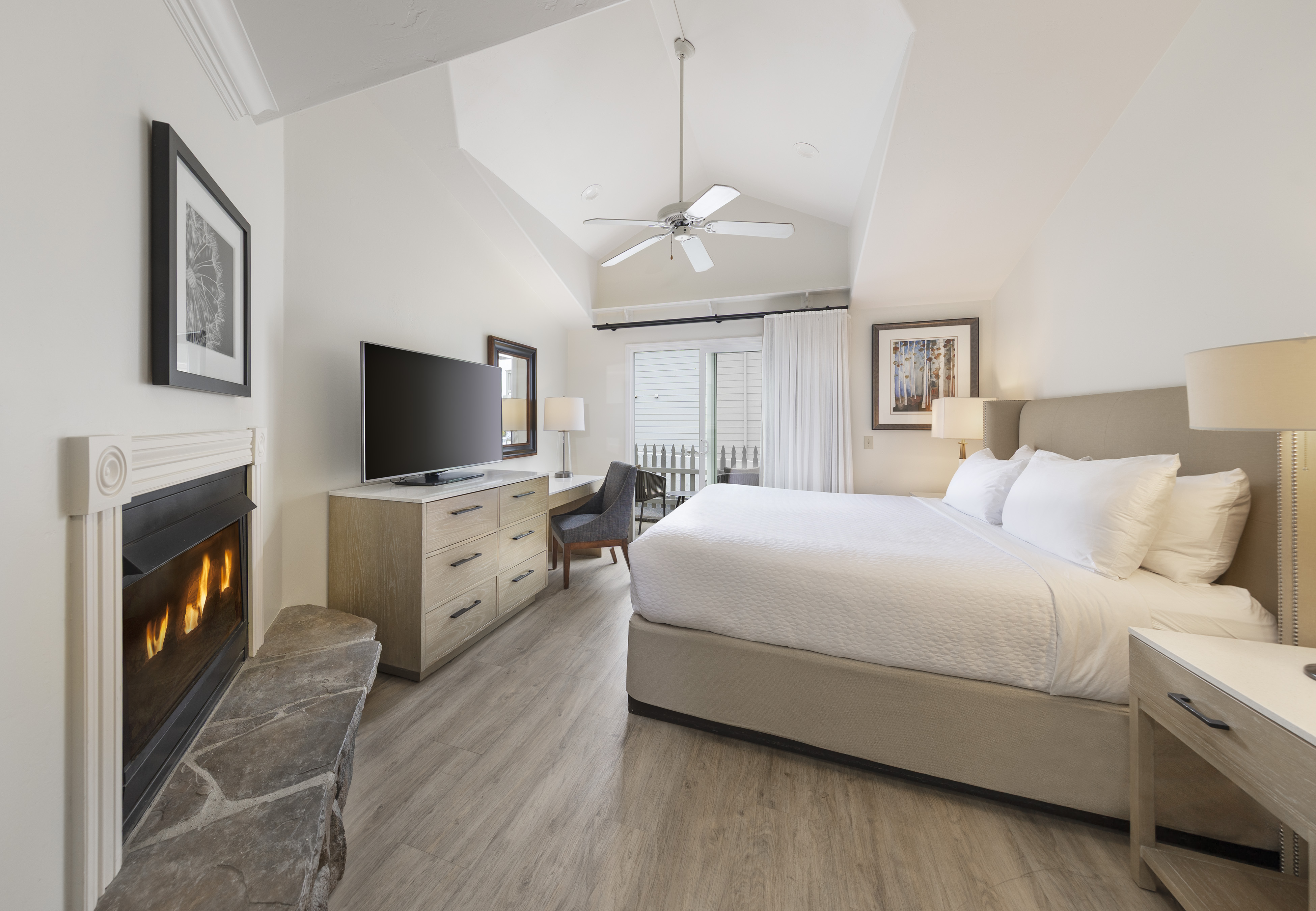 A wide view of a hotel room with a bed, fireplace, TV, and desk.