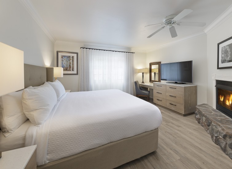 A large hotel room with a king-size bed, fireplace, desk, and TV.