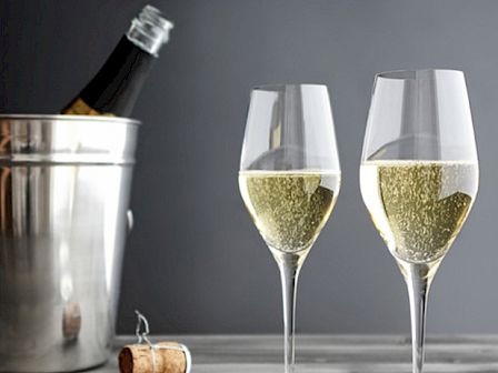 Two champagne flutes half full, a bottle chilling in a metal ice bucket, and a cork on the table, ready to pop.