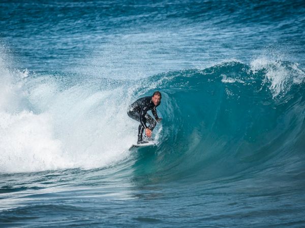 A surfer rides a turquoise wave, carving through the clear water as a white crest explodes beside them.