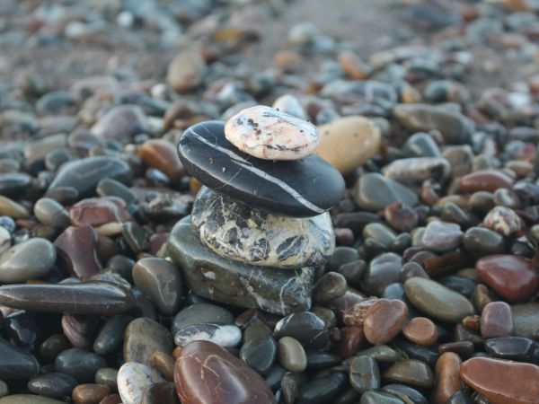 A stack of smooth stones balanced on a pebble beach, with layered rocks and pebbles in various colors.