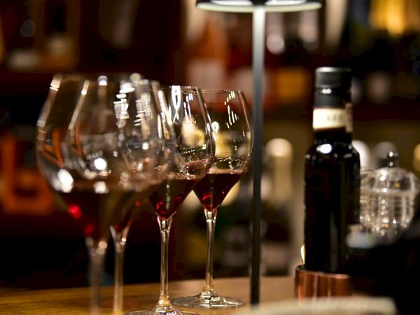 A row of wine glasses with red wine, a bottle, and a dim bar setting&mdash;glasses gleam under warm lighting, ready for tasting.