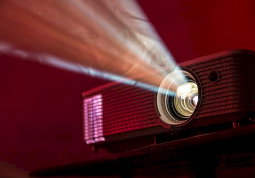 A red projector beams a bright light onto a screen, casting a focused image in a dark, moody room.