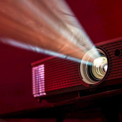 A red projector beams a bright light onto a screen, casting a focused image in a dark, moody room.