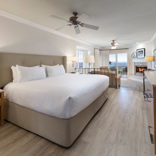 A spacious hotel room with a large king bed, nightstands, a sitting area, work desk, flat-screen TV, and warm lighting in a modern, airy layout.