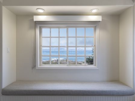 A cozy window nook with a cushioned bench, a large window showing the ocean outside, and subtle built-in lighting ending with a view.