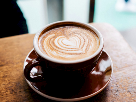 A cup of latte with latte art heart on a wooden table, cozy cafe vibe, warm tones, top view, ends with a period.